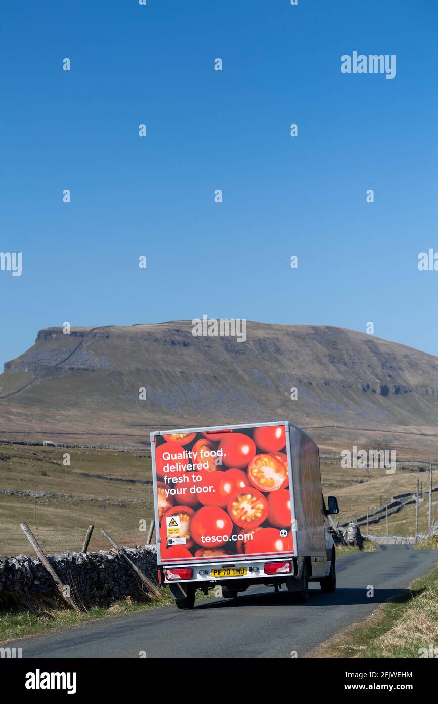 Tesco home delivery van travelling down a rural road in the Yorkshire Dales, with Penyghent Fell in the background. Yorkshire Dales National Park, UK. Stock Photo