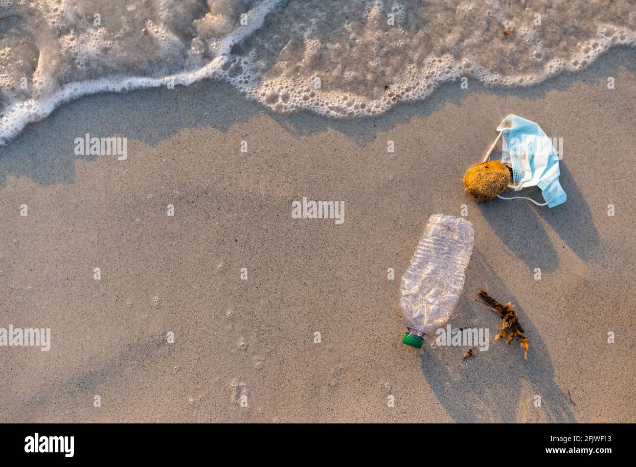 Top view waste on the beach shore. Plastic bottle and face mask. Environmental conservation and pollution concept. Stock Photo