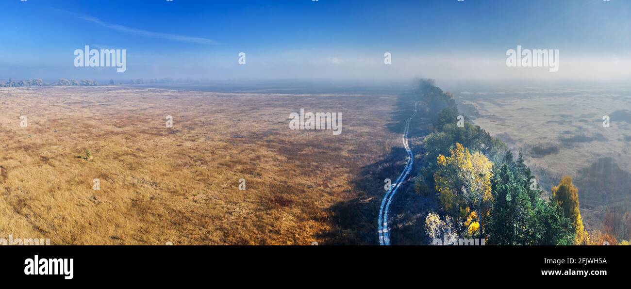 The road passing between autumn fields and forest belts. Aerial view. Nature autumn background. Stock Photo