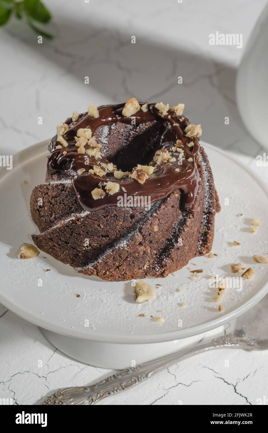Brownie cake poured with chocolate and nuts on a white stand with hard light Stock Photo