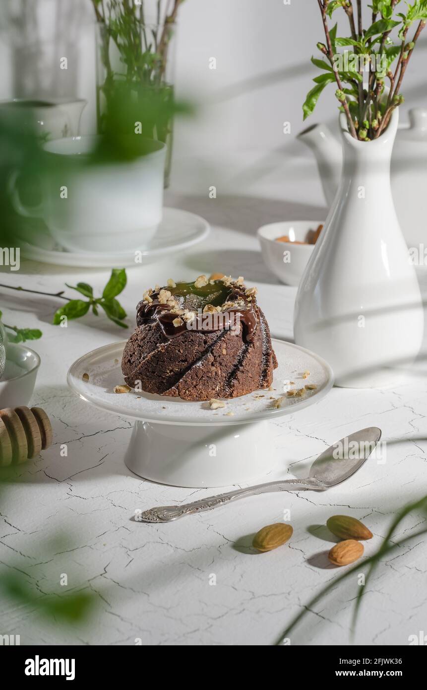 Brownie cake poured with chocolate and nuts on a white stand with hard light Stock Photo