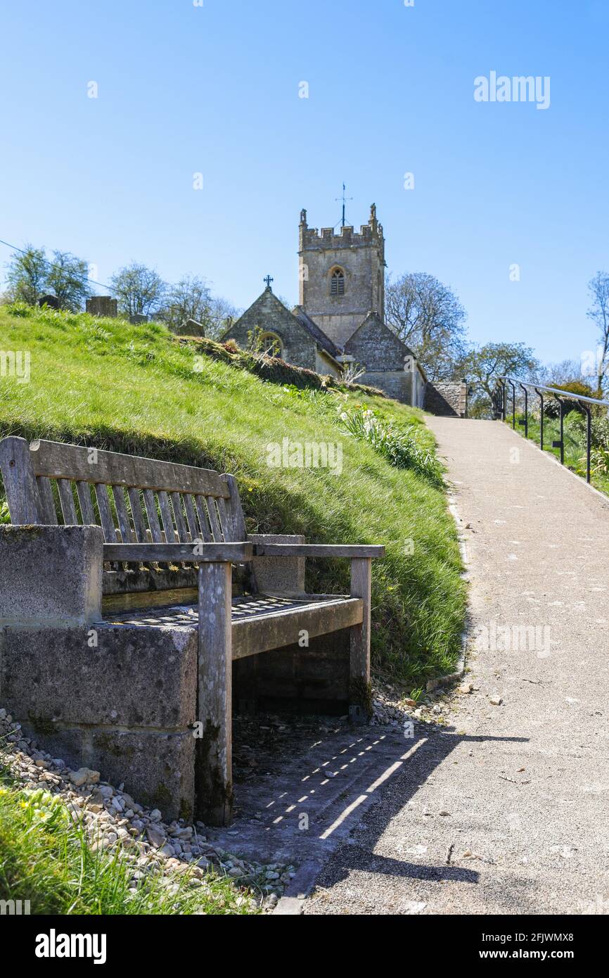 A wooden bench seat as a resting place on the way to St Oswald's church in the Cotswold village of Compton Abdale in Gloucestershire UK Stock Photo
