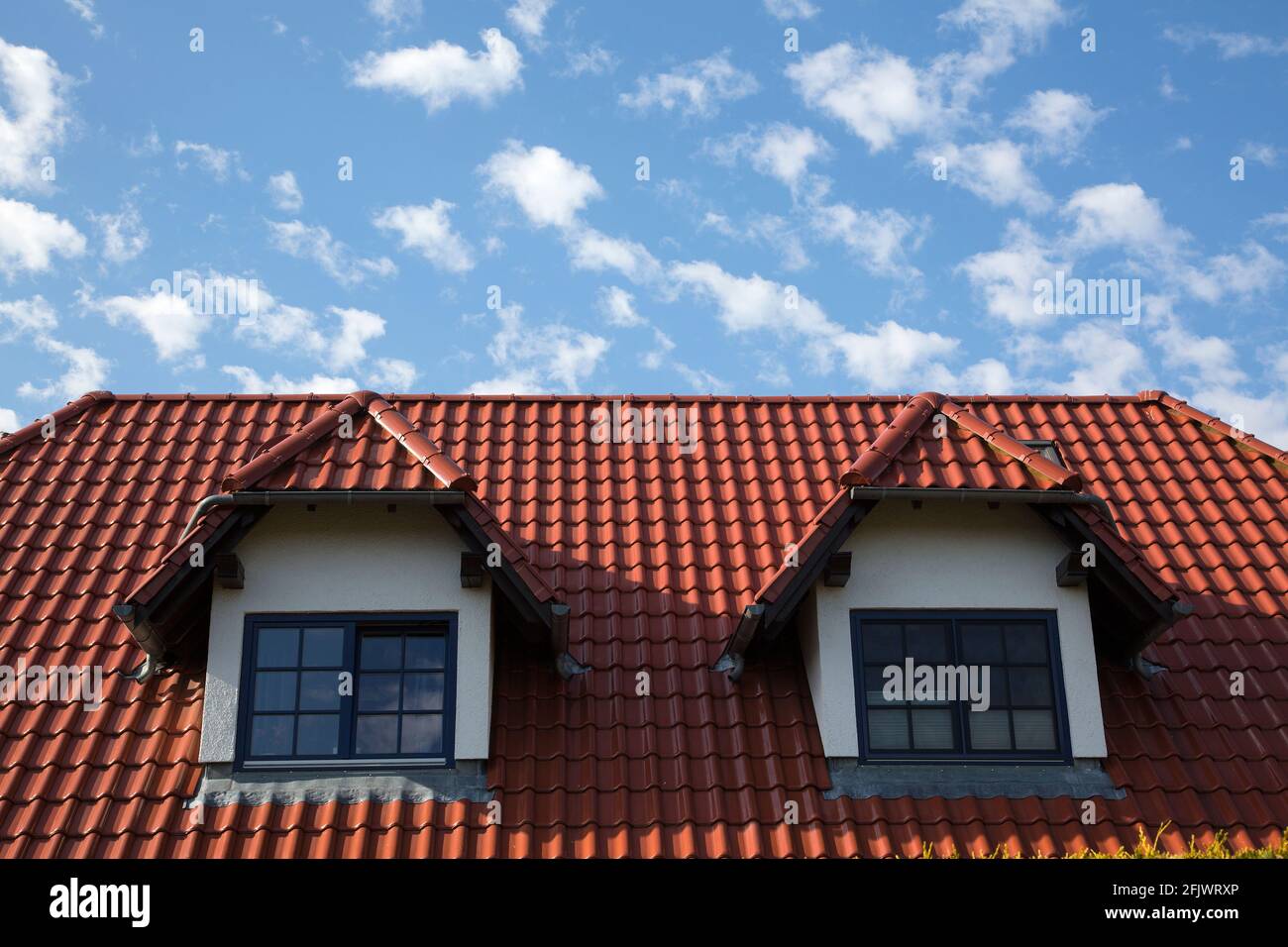 Red tiled roof with two dormers in front of a blue sky with clouds Stock Photo