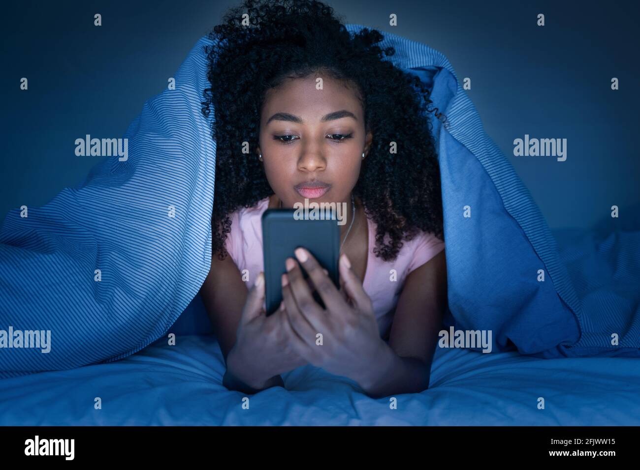 Sleepy woman lying in bed under the blanket using smartphone at night Stock Photo Alamy