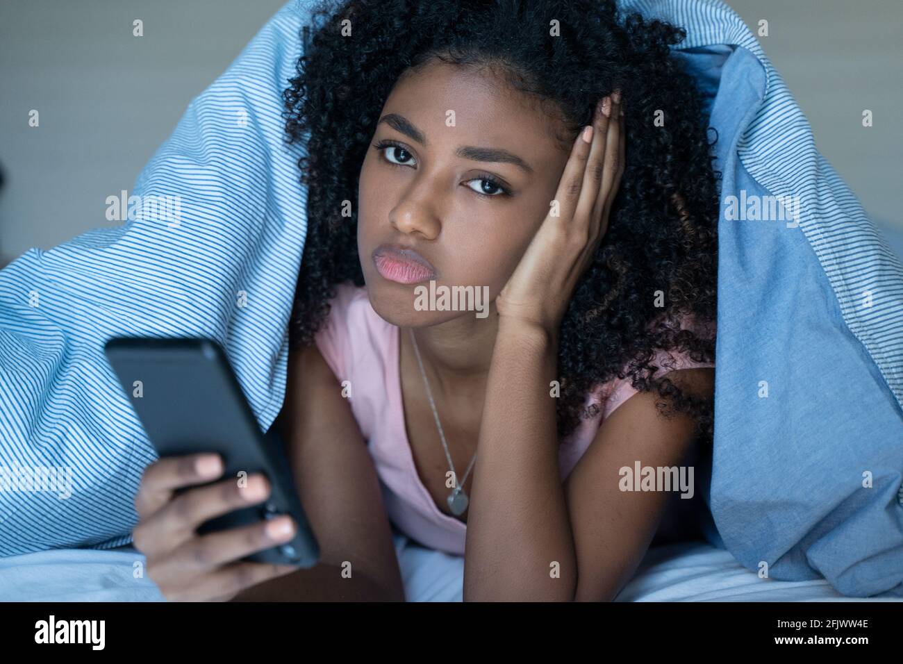 Sleepy woman lying in bed under the blanket using smartphone at night Stock Photo Alamy
