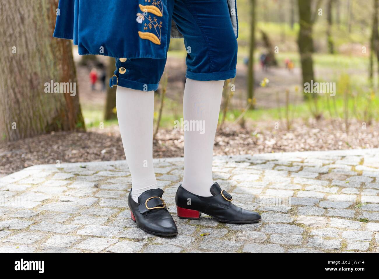 Details of a man's dress in a baroque costume. White stockings and black shoes, golden buttons, decorative hems. A man standing on a cobbled walkway Stock Photo