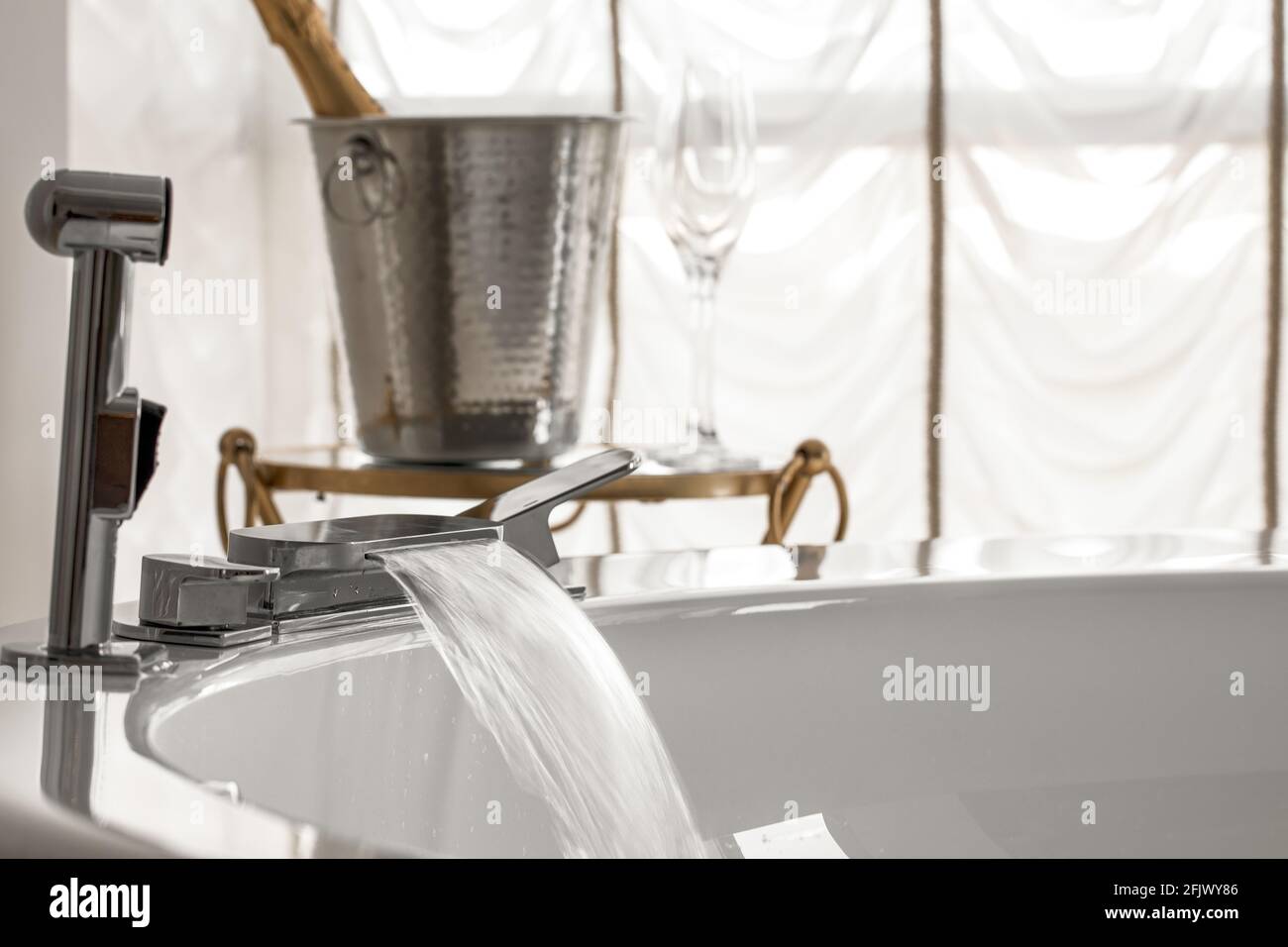 Spout running water from wide bath tube faucet into a hot Jacuzzi with