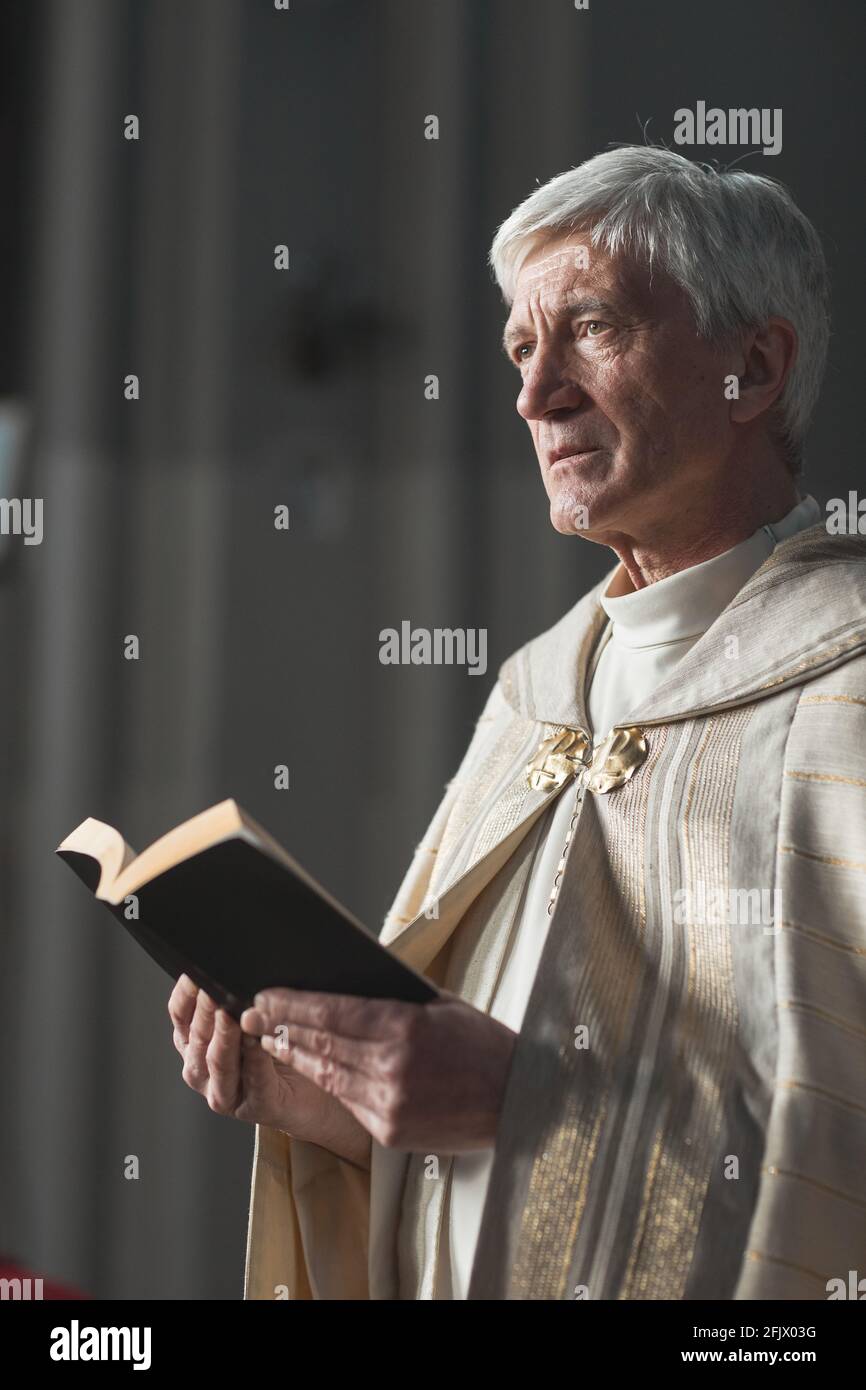 Senior priest standing with Bible and reading prayers during wedding in