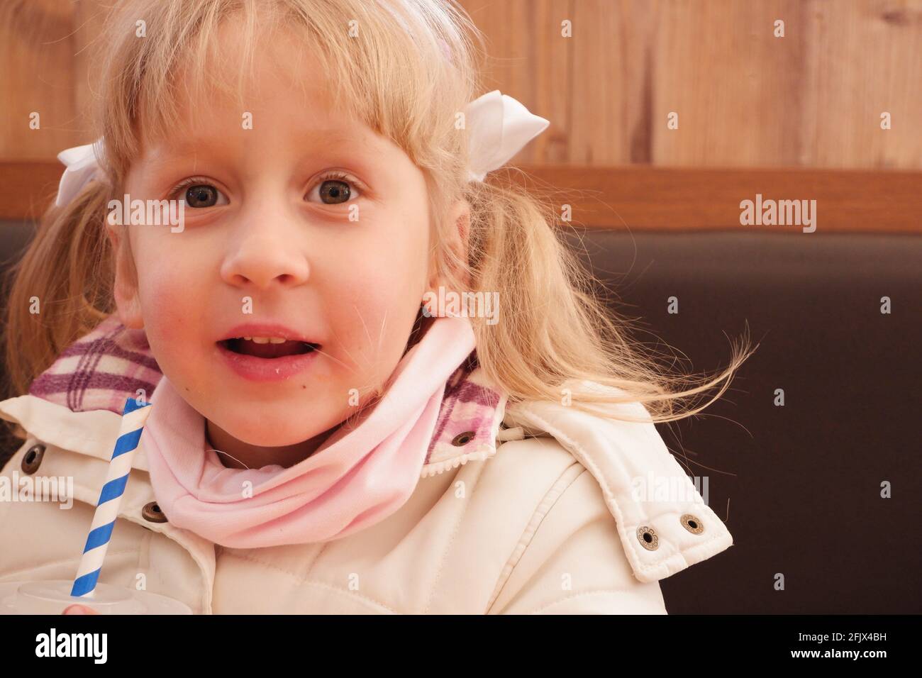 A little girl in a cafe drinks a drink from a striped tube Stock Photo