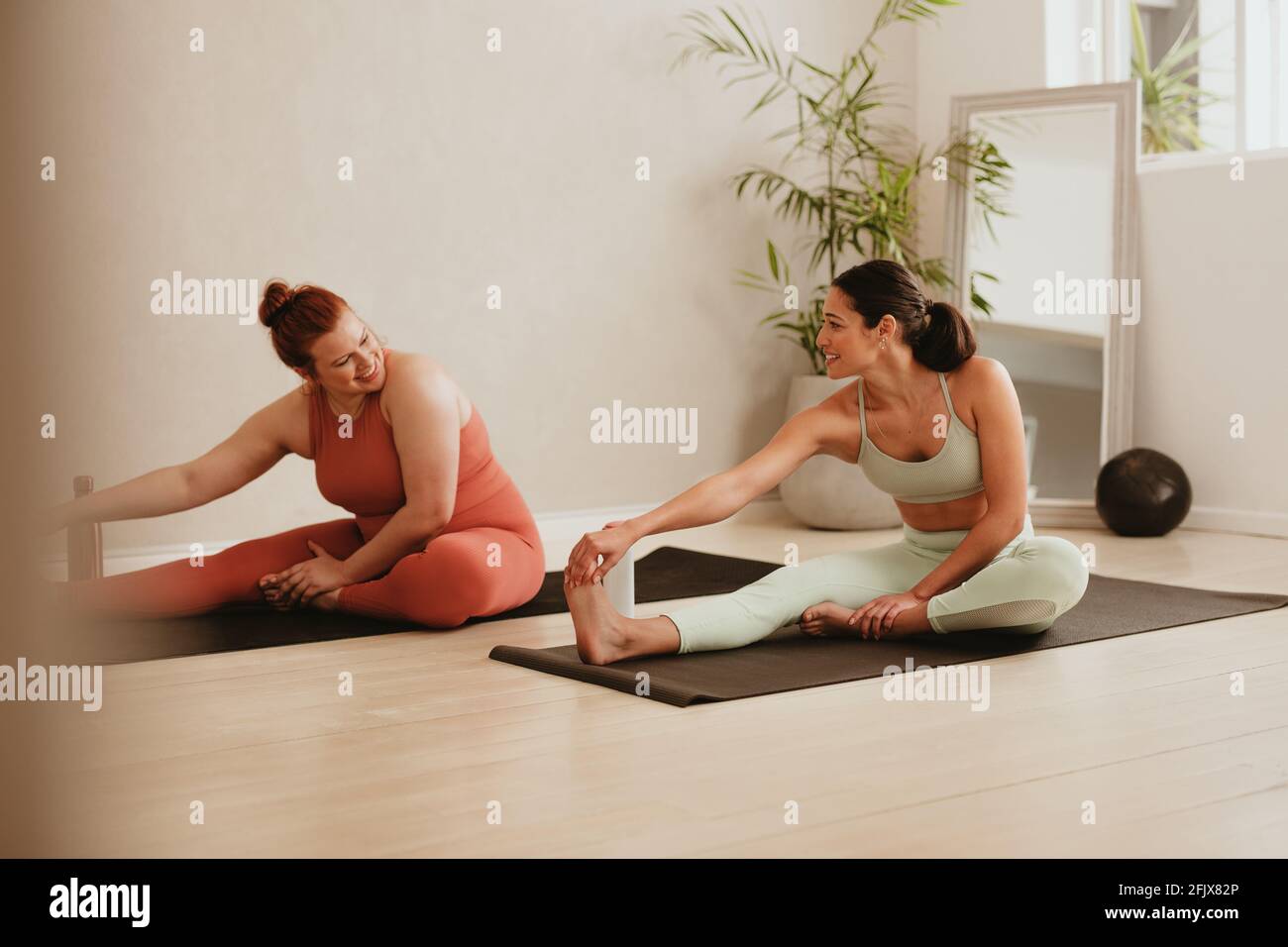 Two females exercising together in fitness studio. Women in sports clothing doing leg stretching workout at gym. Stock Photo