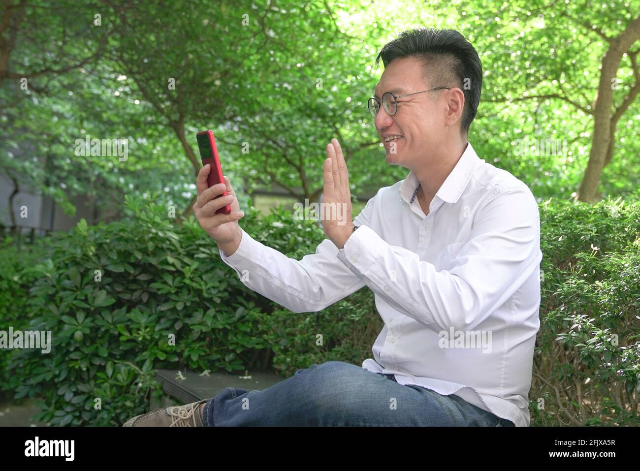 Asian businessman waving his hand, having video chat using his smartphone, outdoors. Stock Photo