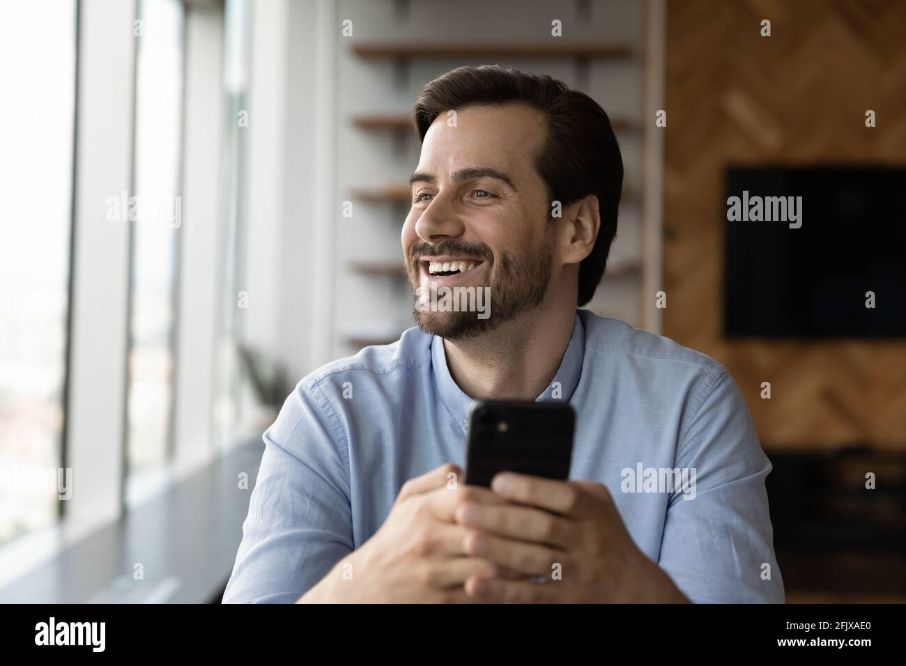 Smiling young man use cellphone looking in distance Stock Photo
