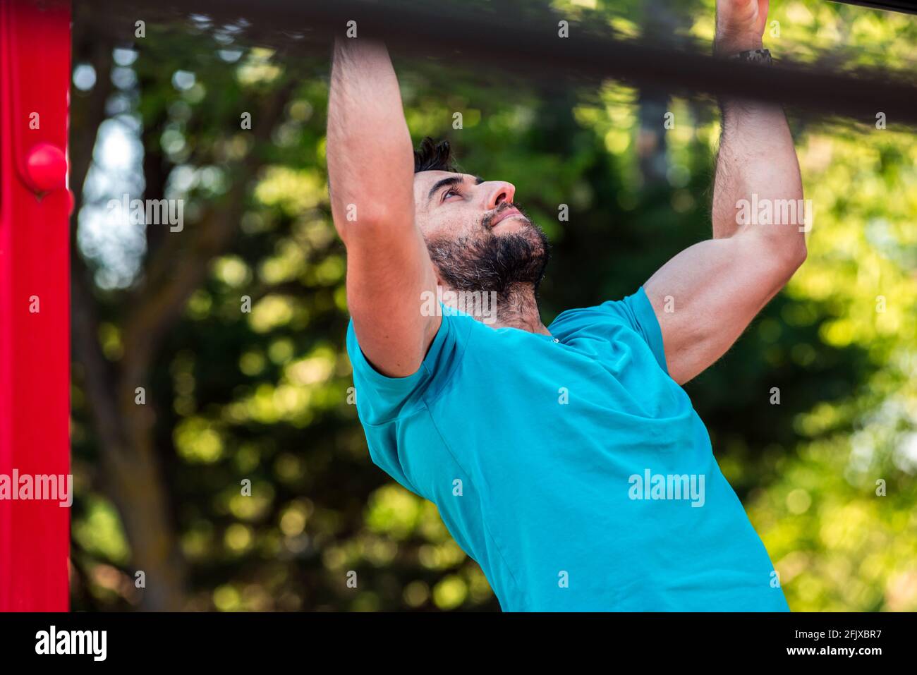 Dark-haired athlete with beard doing a pull-up on a calisthenics bar. Outdoor crossfit concept. Stock Photo