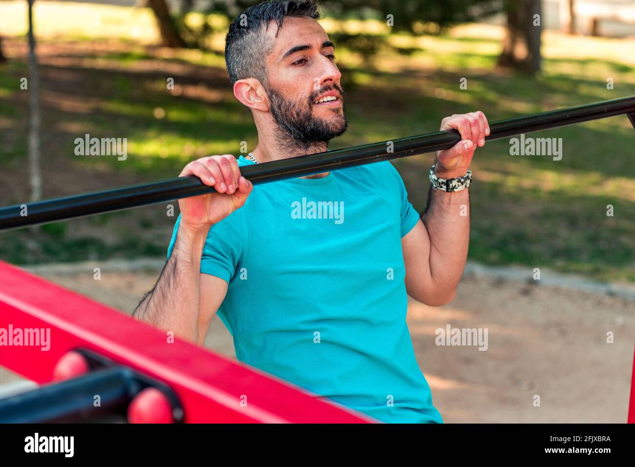 Top view of a Dark-haired athlete with beard doing a pull-up on a calisthenics bar. Outdoor crossfit concept. Stock Photo