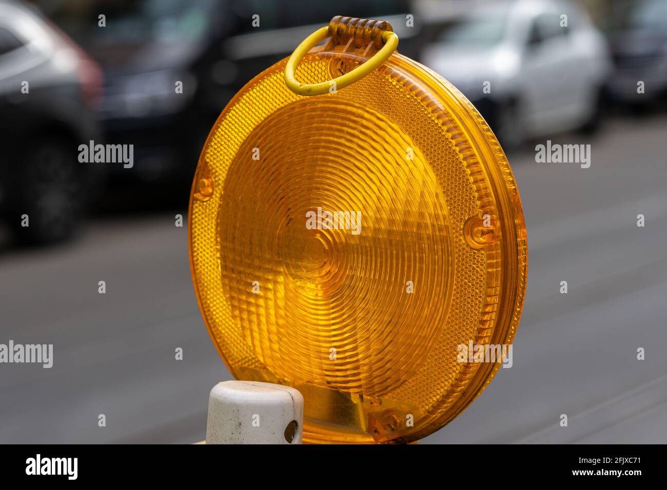 Closeup of a circular yellow warning light in the street with cars in