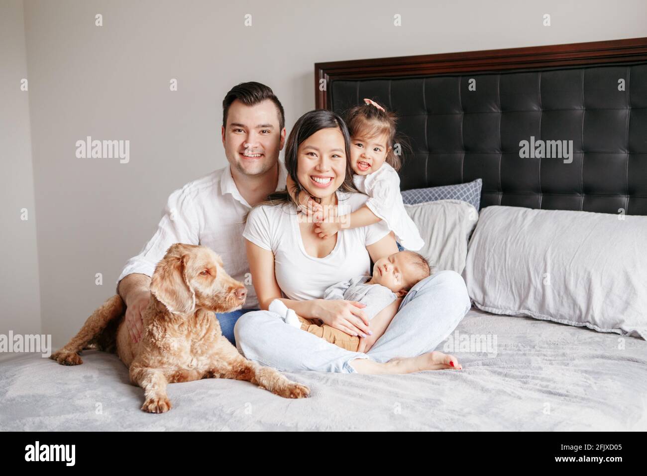 Happy multiracial young family with children kids and dog pet on bed. Stock Photo