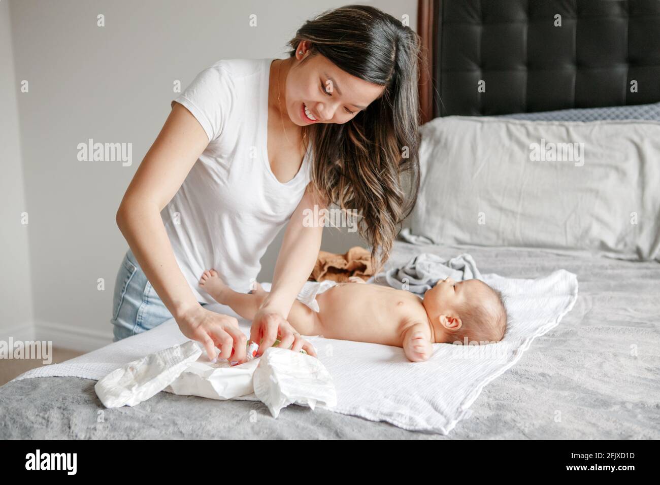 Asian busy mother changing diaper clothes for newborn baby son at home Stock Photo