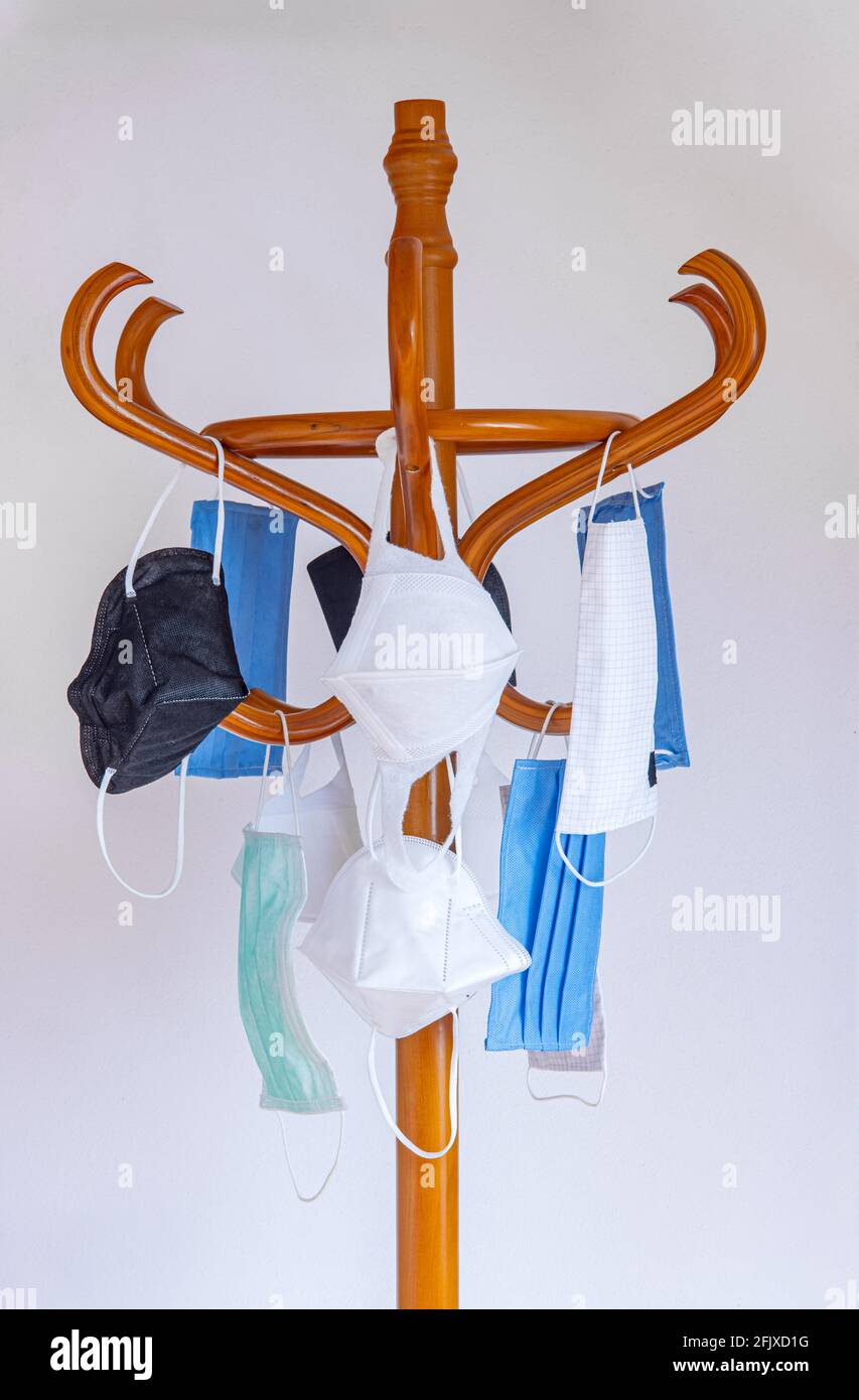 The used protective face masks hanging on a wooden coat rack, white wall background. Stock Photo