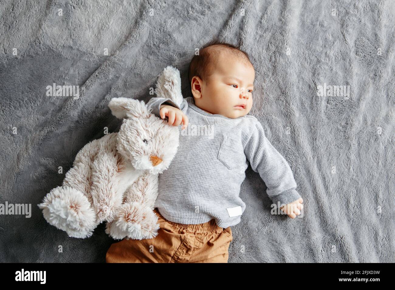 Two months newborn Asian baby boy lying on bed with rabbit comfort toy Stock Photo