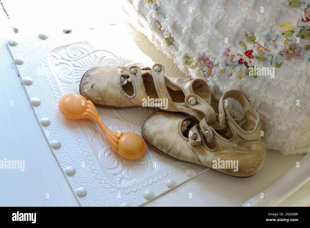 Antique baby shoes and rattle by floral and fringed pillow.jpg Stock Photo
