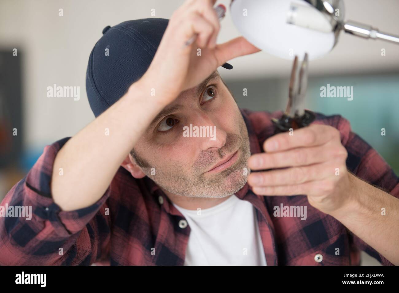 a man fixes the lamp with a screwdriver Stock Photo
