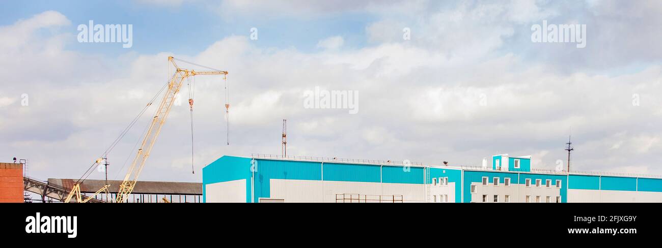 Machine crane at a construction site with a warehouse in an industrial area, panoramic view, high resolution. Stock Photo