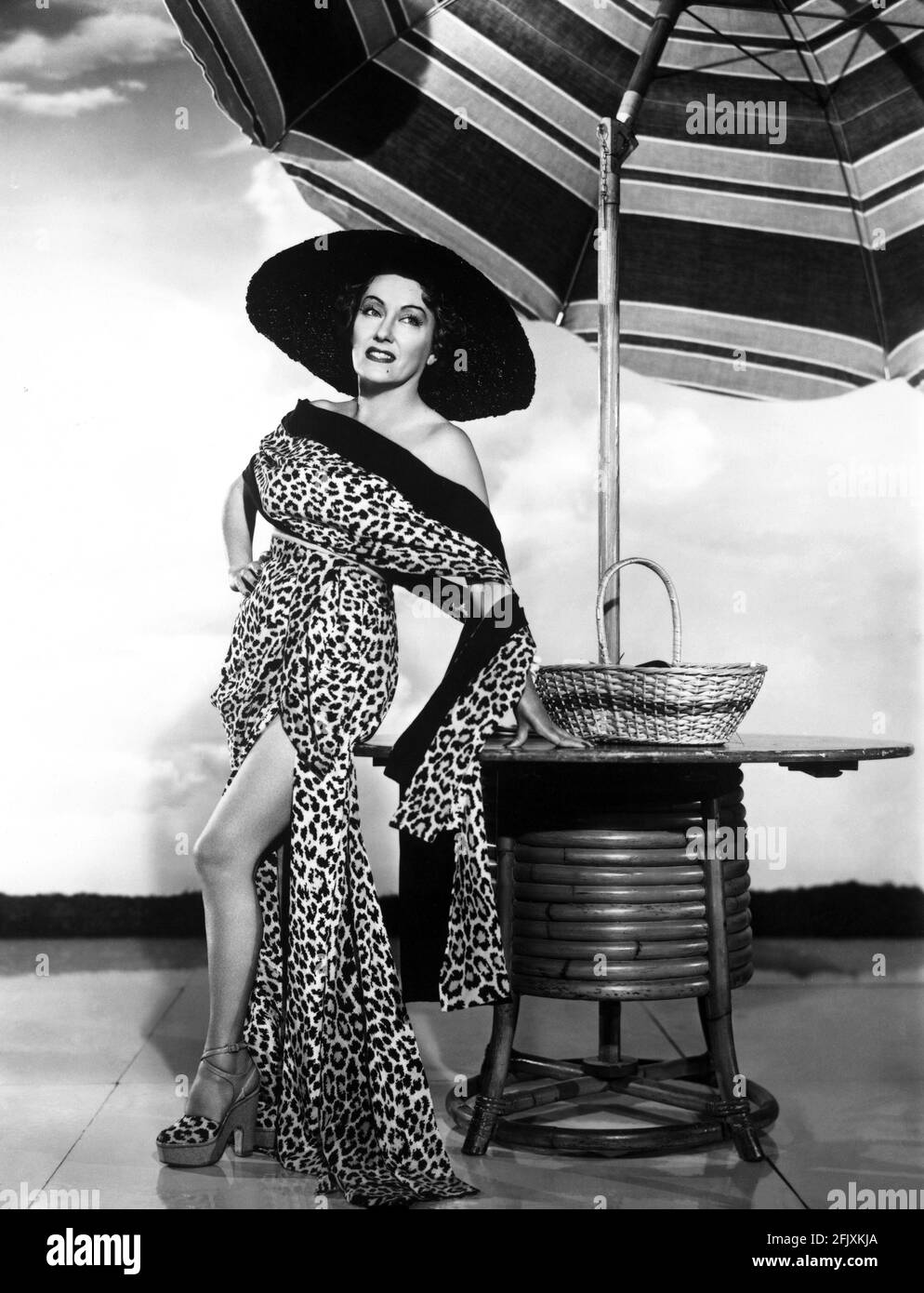 1951 , USA : The movie actress GLORIA SWANSON ( 1898 - 1983 ) as Norma Desmond in SUNSET BOULEVARD ( Viale del Tramonto ) by Billy Wilder, costume by Edith HEAD , Paramount pubblicity still - FILM - CINEMA - attrice cinematografica - leopardo - leopardato - maculato - VAMP - leopard - leopard-skin - leoparded - sandali - sandals - bambou - cappello di rafia - hat - neo - mole - spalla - spalle - shoulder - shoulders - ombrellone da spiaggia - beach-umbrella - leggy pose - gambe - gamba - leg - legs - giardino - garden - DIVA - DIVINA - DIVINE - Hollywood on Hollywood  - copricostume da bagno , Stock Photo