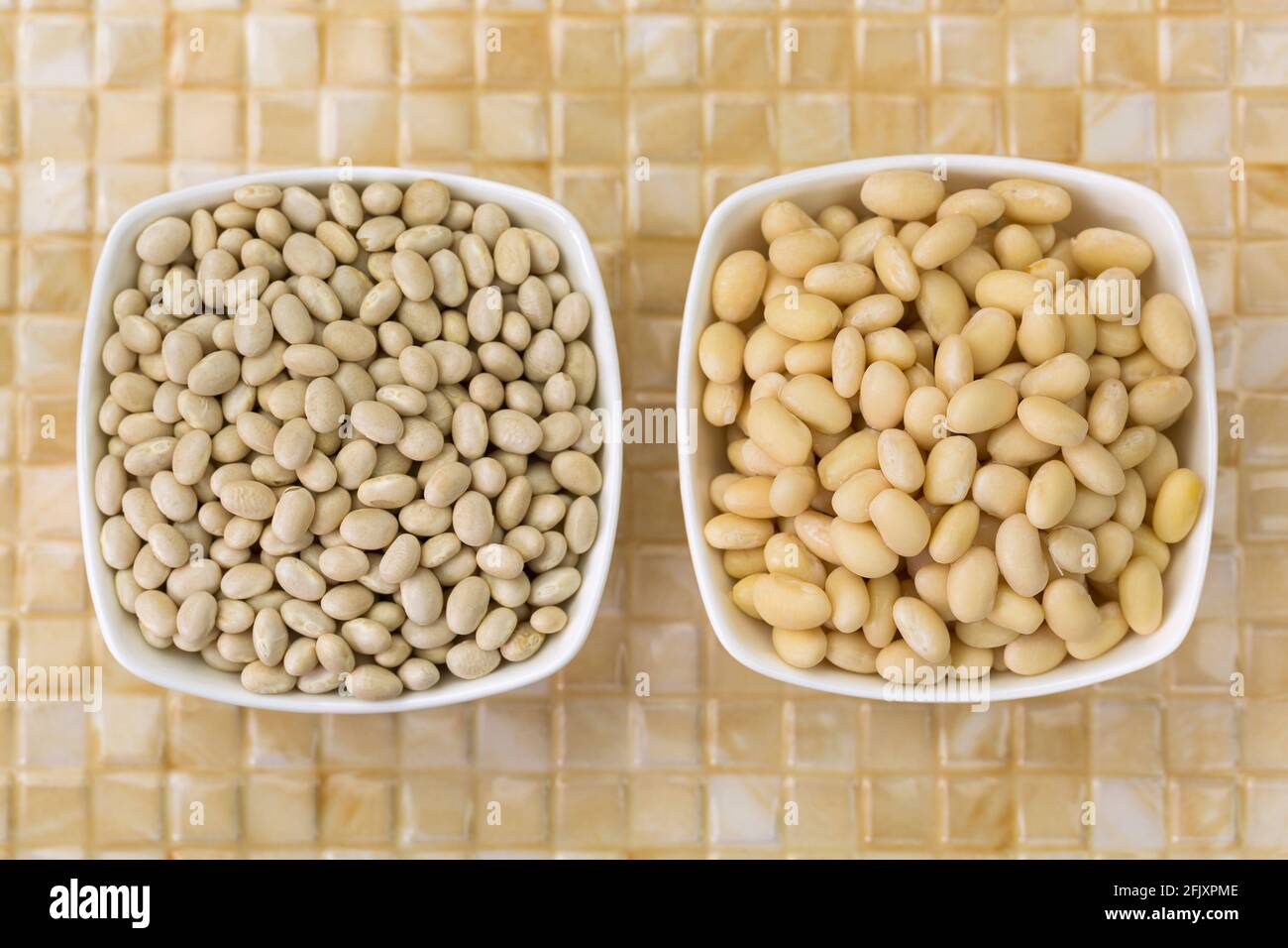 Soaked and dried white pea beans, Navy bean, Pearl Haricot, Boston bean in white bowl on yellow ceramic background, top view (Phaseolus vulgaris) Stock Photo