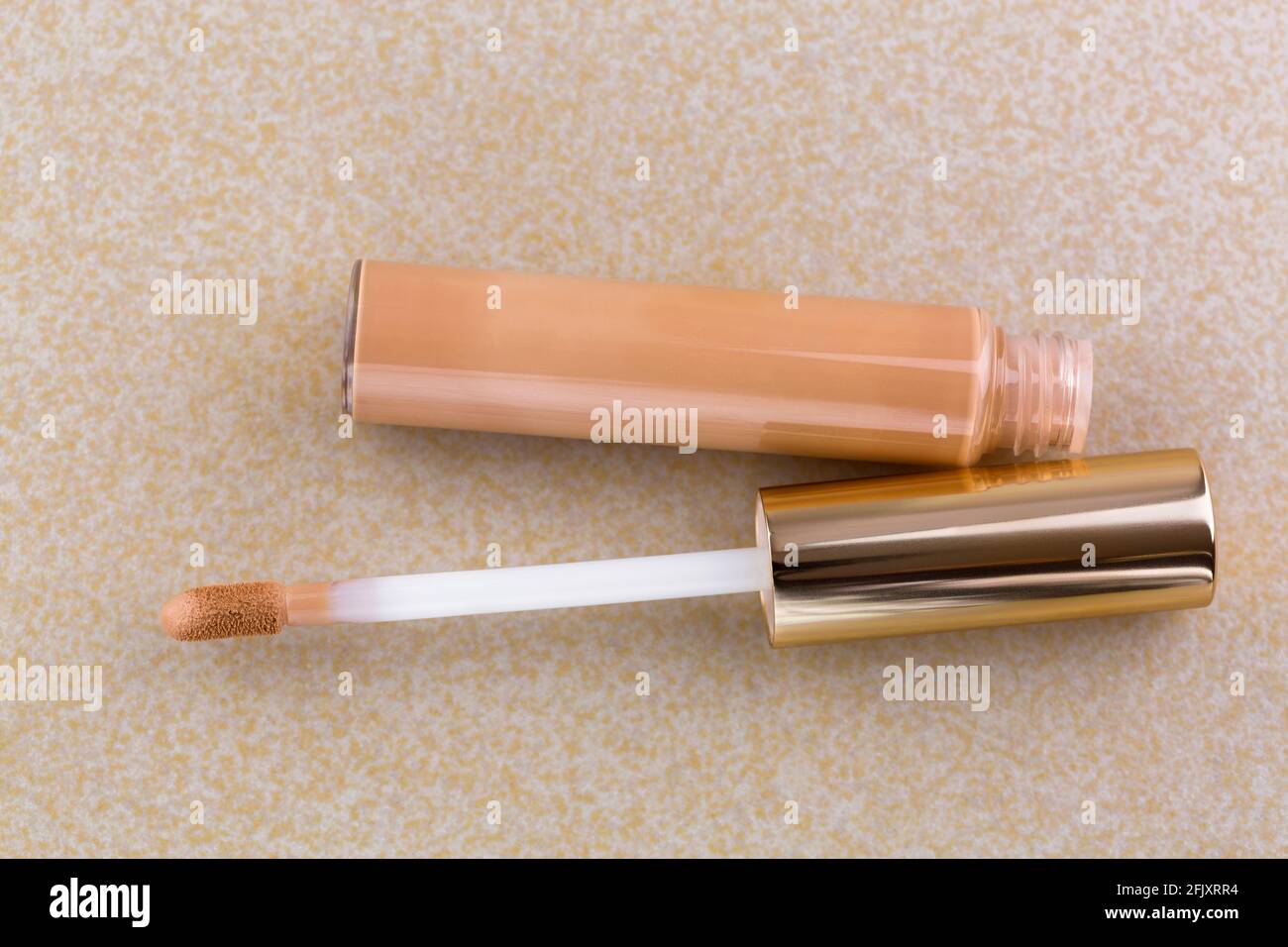 Tube of flawless wear creamy concealer with doe-foot applicator, high cover to conceal spots, blemishes, on yellow tile background Stock Photo