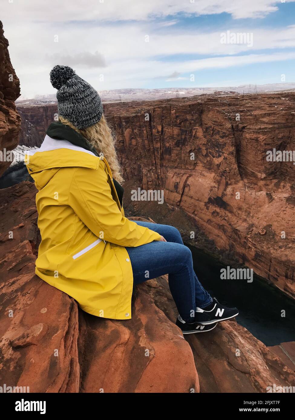 Woman sitting on the rocks of the Grand Canyon National Park in Arizona. Woman wearing a yellow rain jacket and black new balance sneakers. Stock Photo