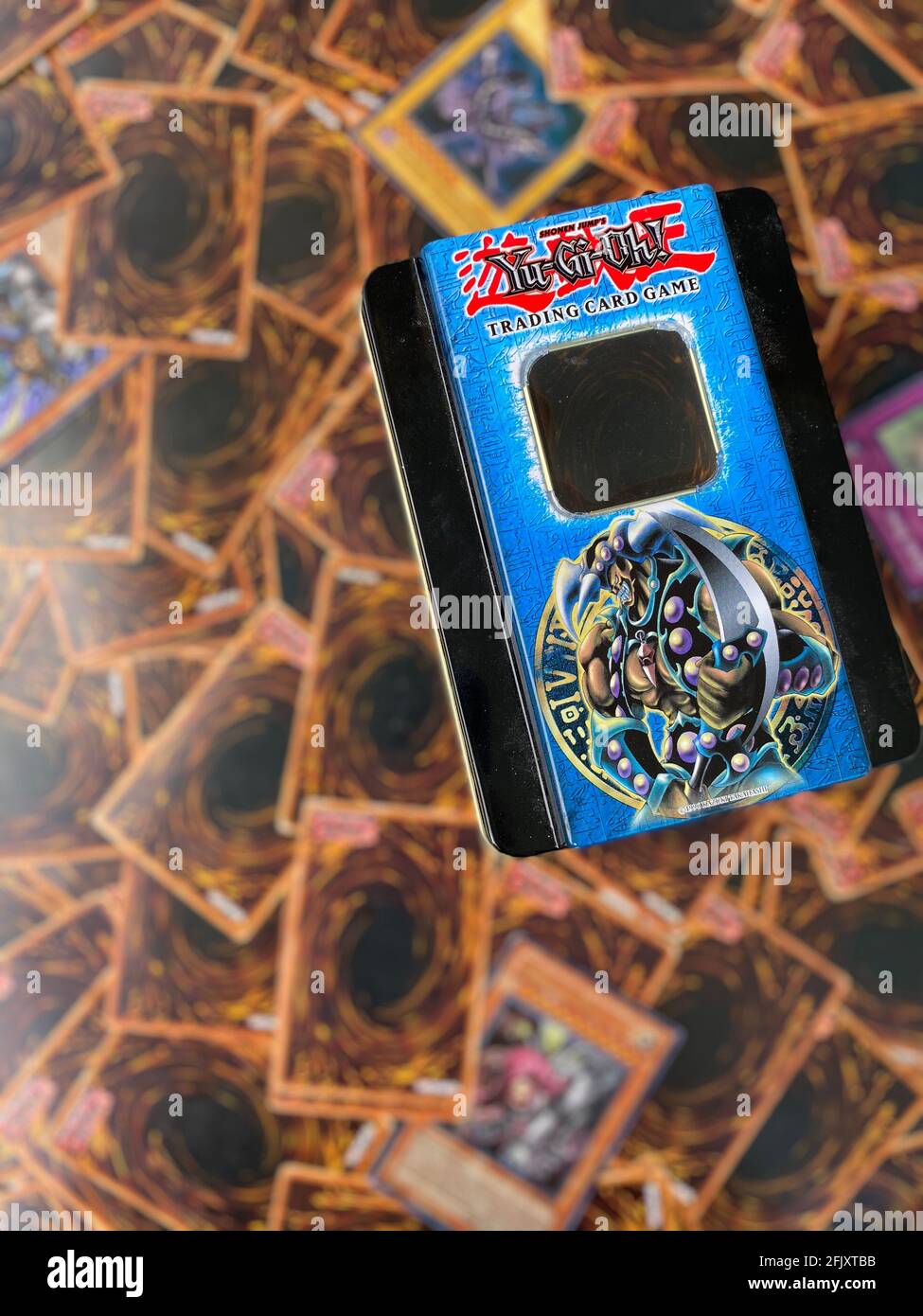 Yu-gi-oh also spelled Yugioh card game tin box that shows different player cards blurred out in the background. Japanese card game by Konami. Stock Photo