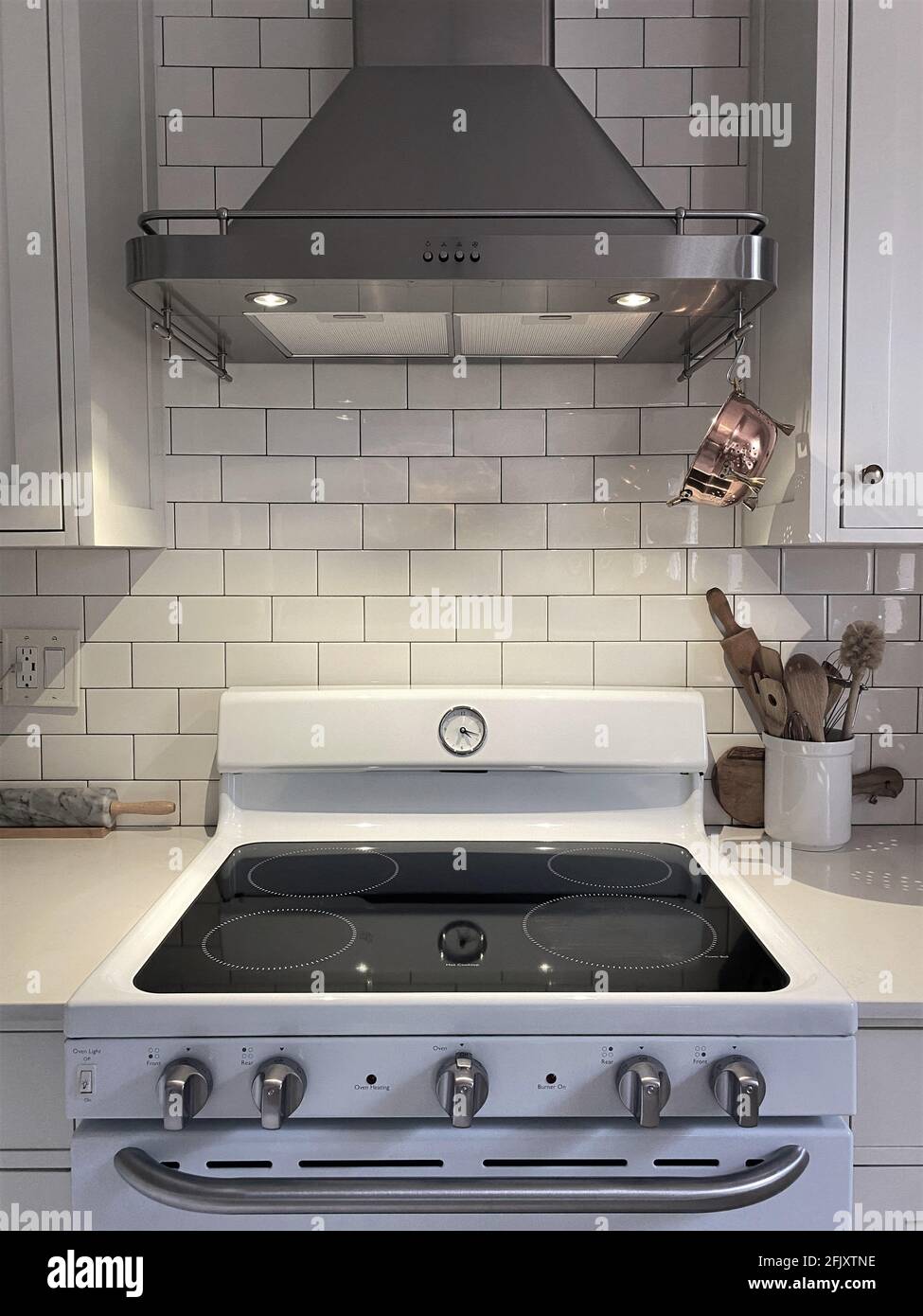 White Kitchen cupboard with subway tile. Kitchen utensils are in a bowl for cooking with small vintage copper colander hanging. Kitchen hood exhaust. Stock Photo