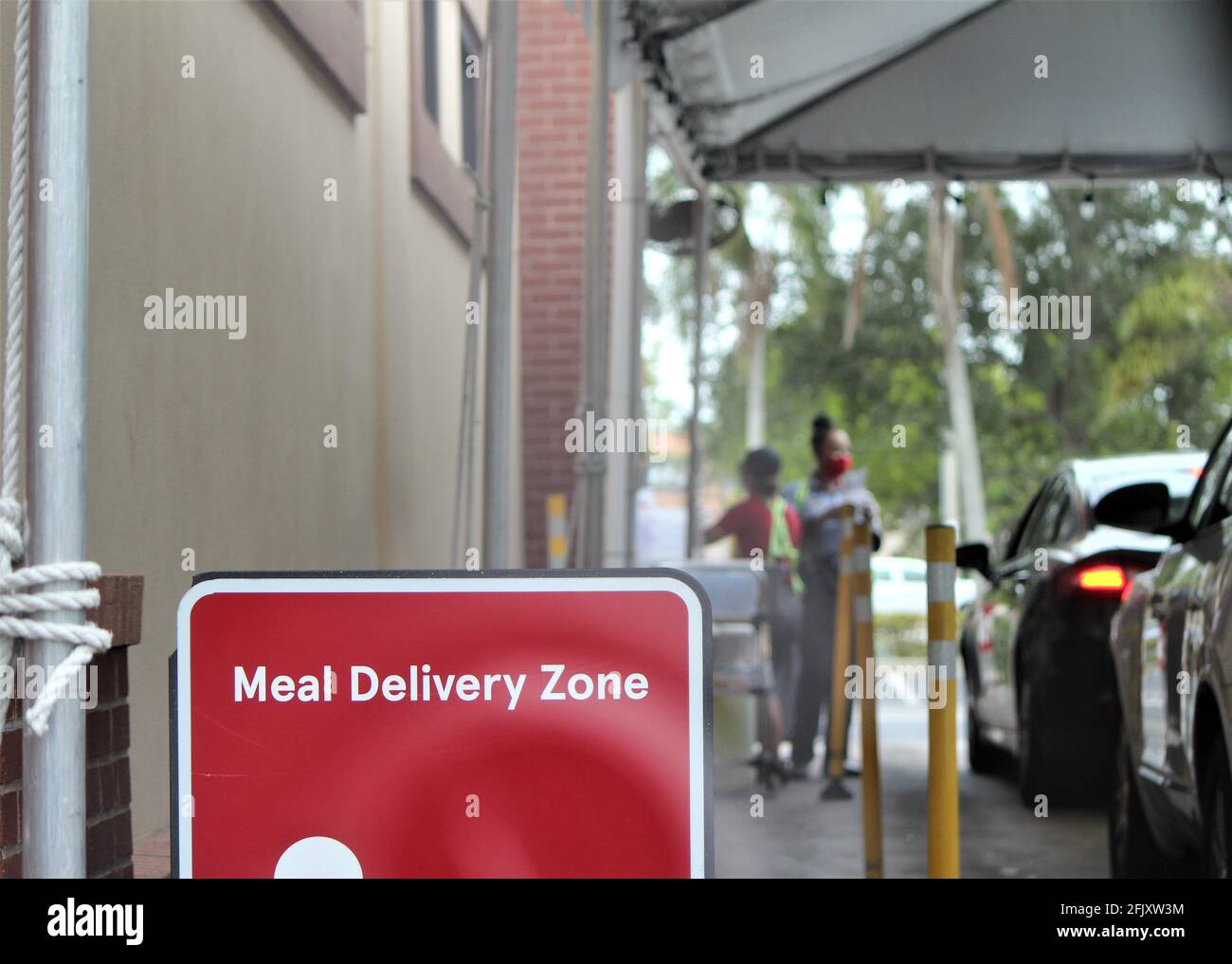 Meal Delivery Zone sign with a car line for food pick up. Workers