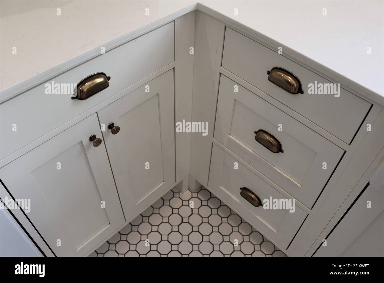 Corner kitchen with white countertop and cabinets and textured tile floors. Small vintage bronze handles for opening and closing the doors. Farm house Stock Photo