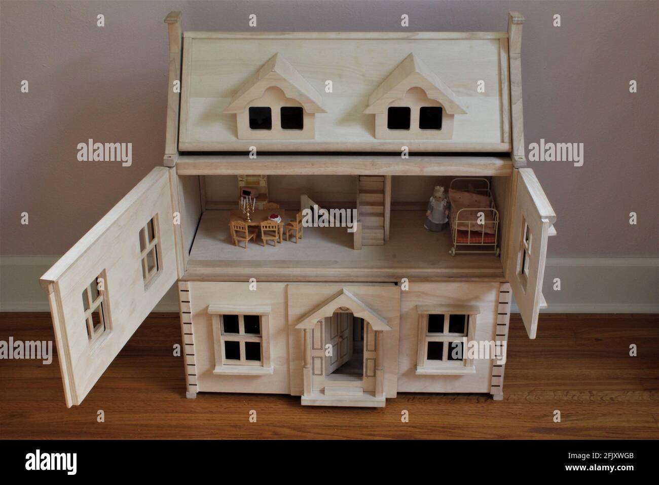 A DIY wooden doll house in a child's room to play pretend. The doors are open on the second floor and the dolls room is shown with miniature furniture Stock Photo