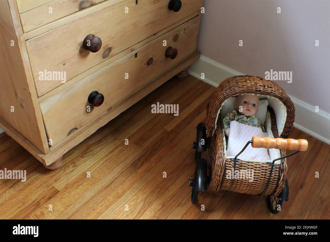 Small woven baby carriage with fake baby inside a play room with wooden floors and cabinets. Stock Photo