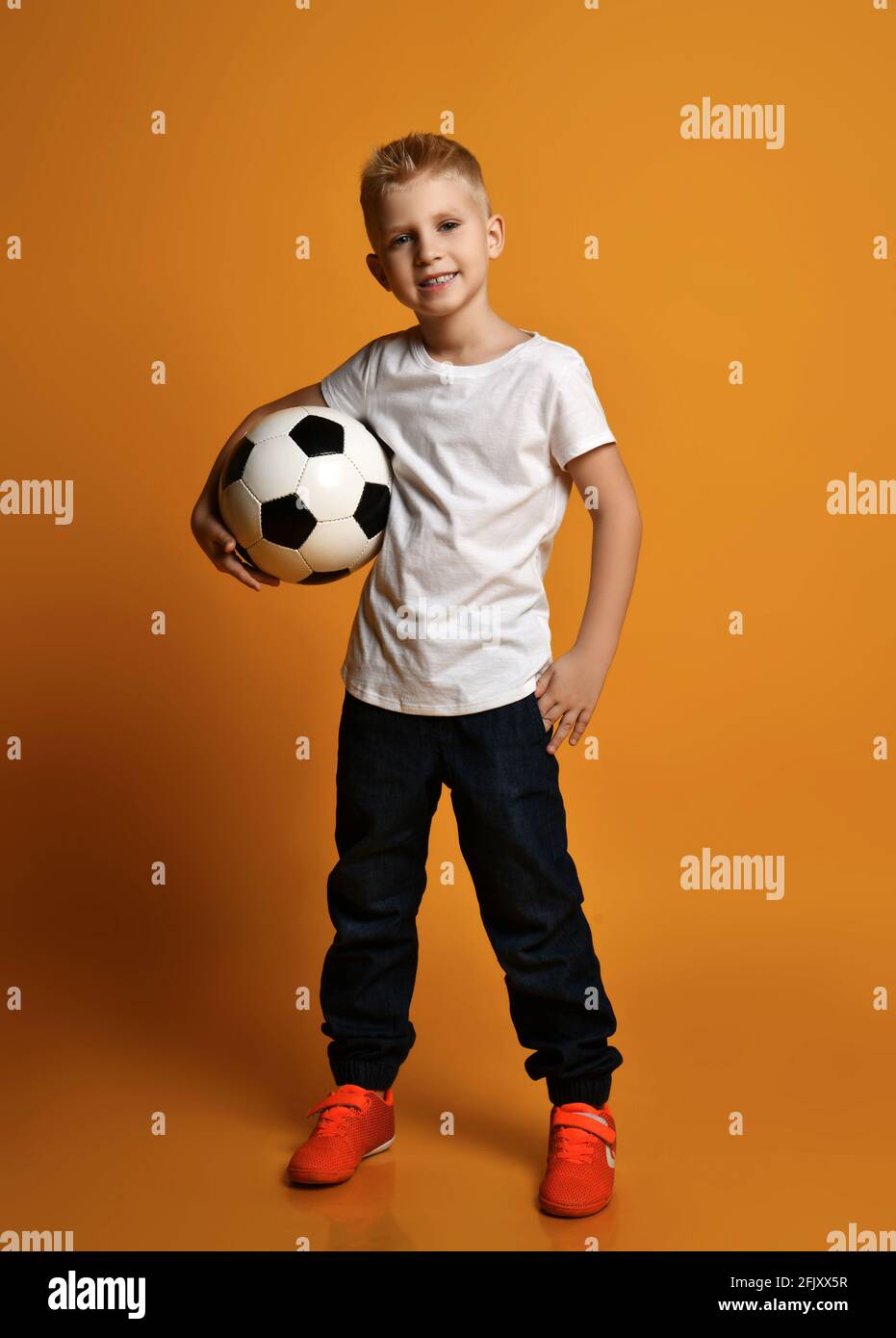 Happy smiling schoolboy, teenager in casual clothes with white blank t-shirt stands holding soccer ball in hand Stock Photo