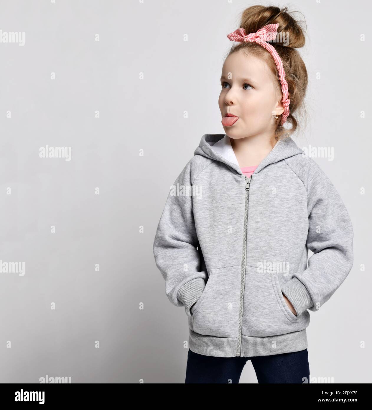 Portrait of naughty frolic kid girl in gray hoodie with zipper standing