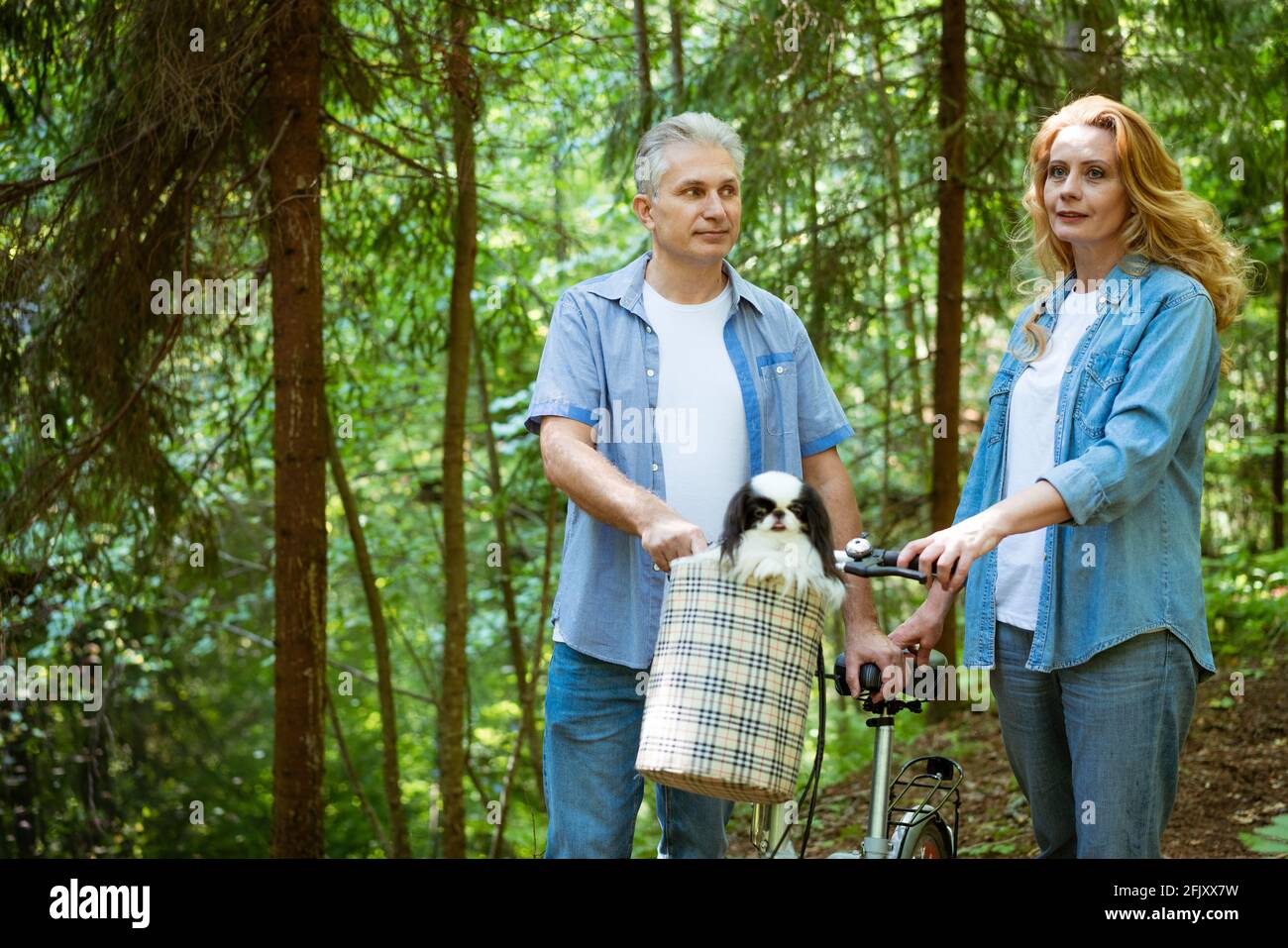 an adult couple in denim clothes on a walk in the woods with a dog that ...