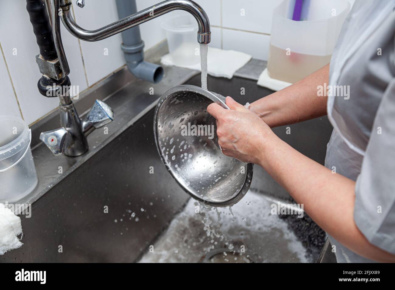 Dishwasher in uniform washes griddle with foam and sponge under the tap