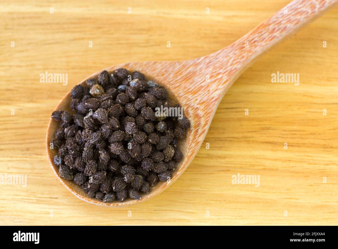 Closeup of air dried papaya seeds in wooden spoon on yellow wood