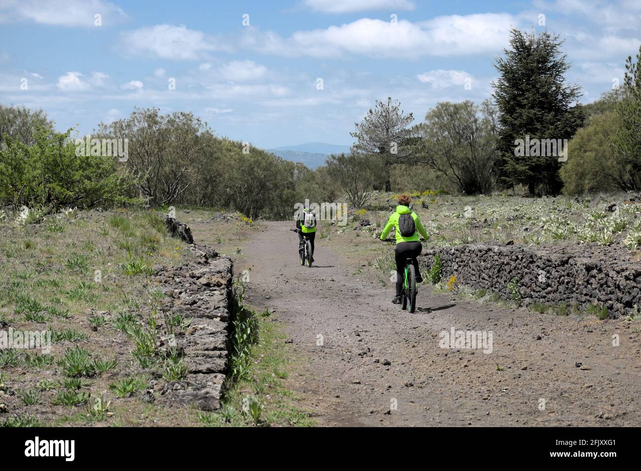 outdoor activity in Sicily nature group of mountain bikers riding along a path of Etna Park Stock Photo