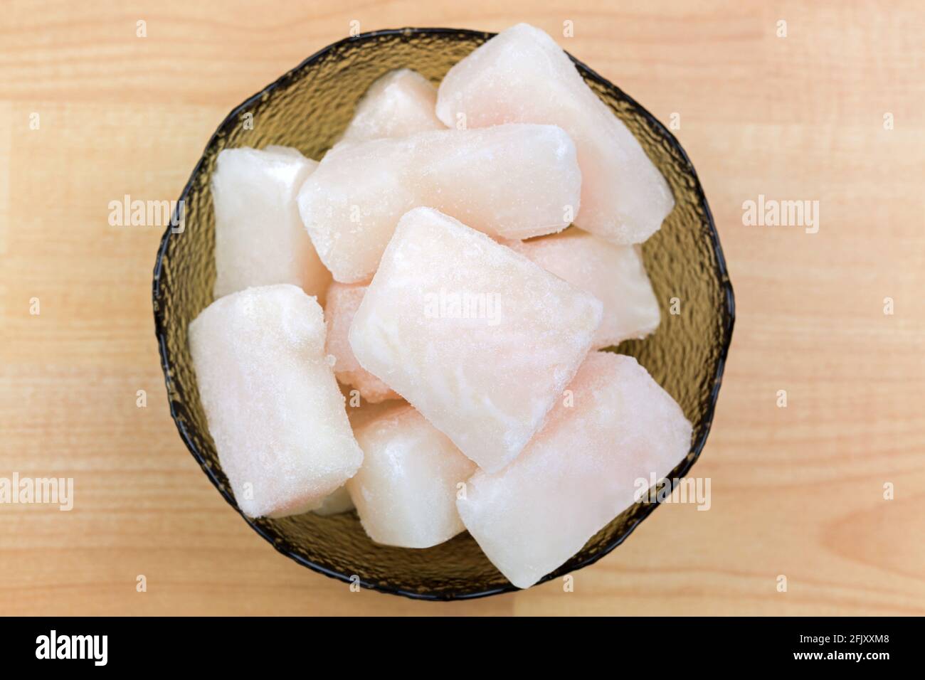 Frozen Pangasius, Dory fish cut in cube in glass bowl, top view. Fillet of fresh water fish in chunk, on a wooden background Stock Photo