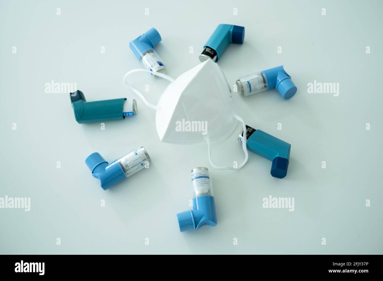 Various asthma spray inhalers and a Covid-19 respirator mask on a white ...