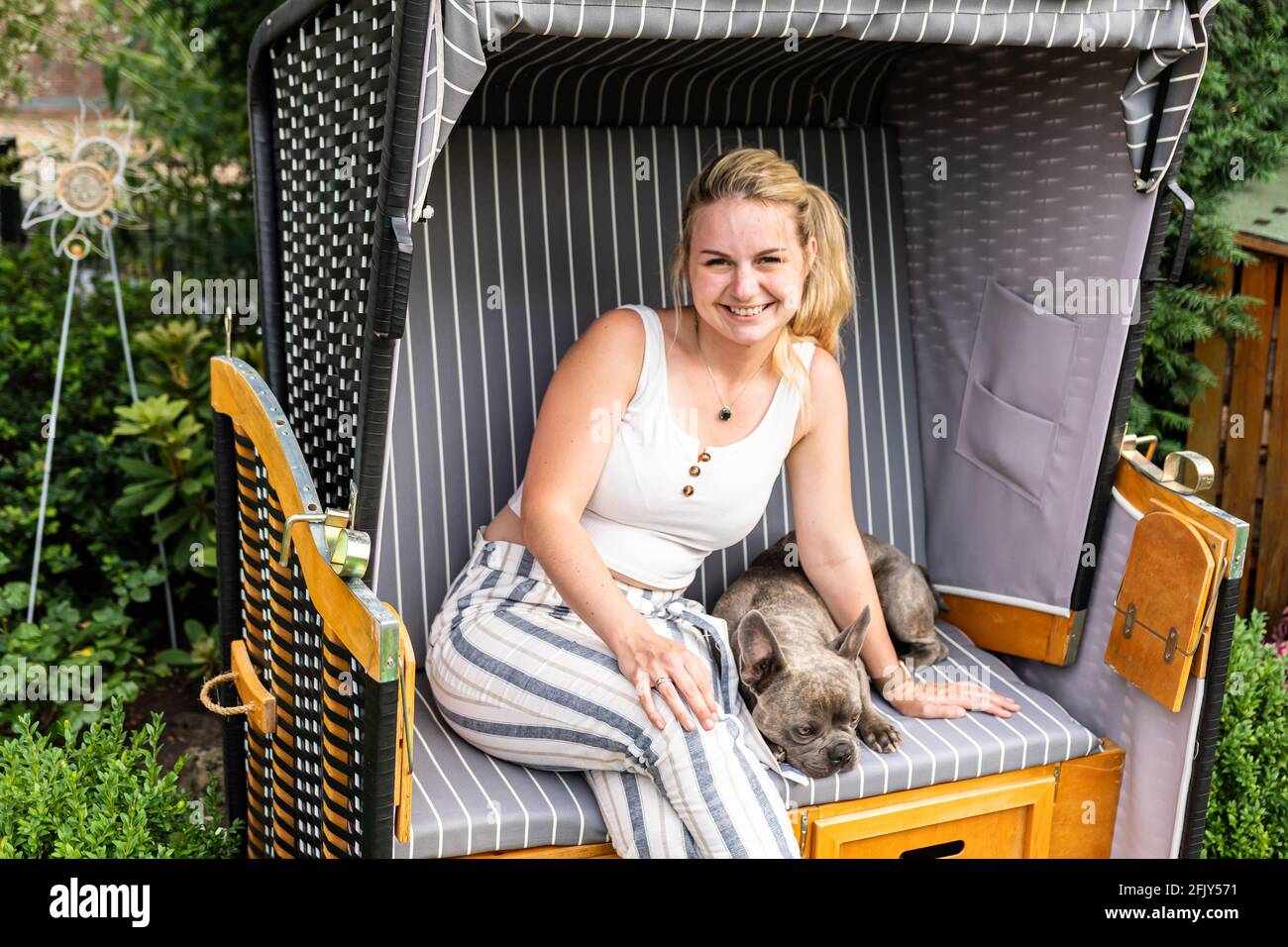 Young blonde woman sitting with her dog in her own beach chair in garden Stock Photo