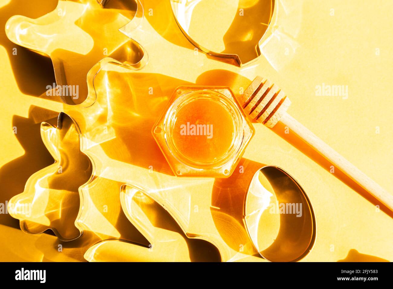 Honey jar, honey dipper and cookie cutters on yellow background. Preparing to bake cookies. Bright sunshine Stock Photo