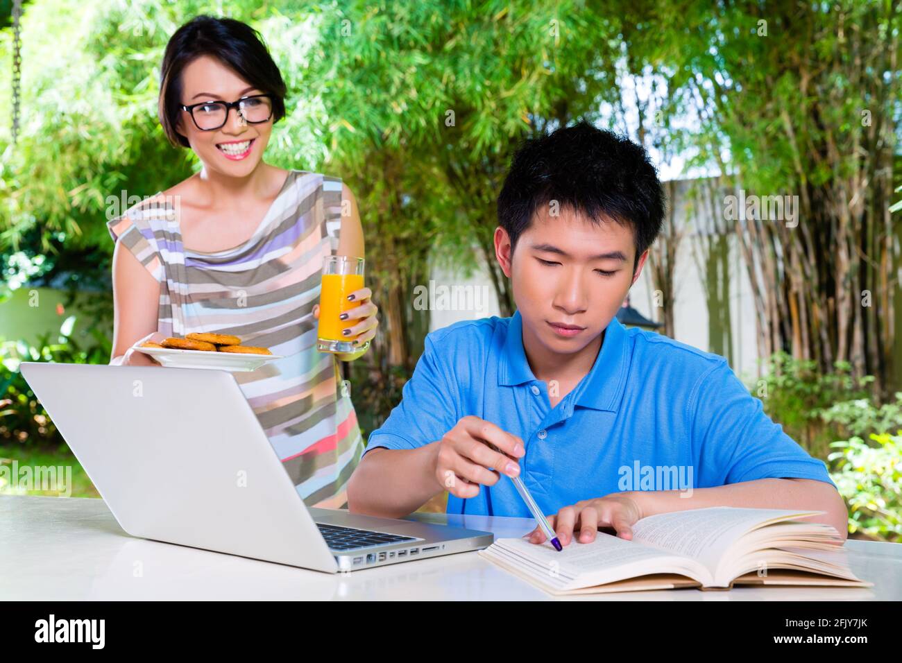 Chinese thoughtful mother brings her son some food, he makes homework for the next day at school and is concentrated Stock Photo