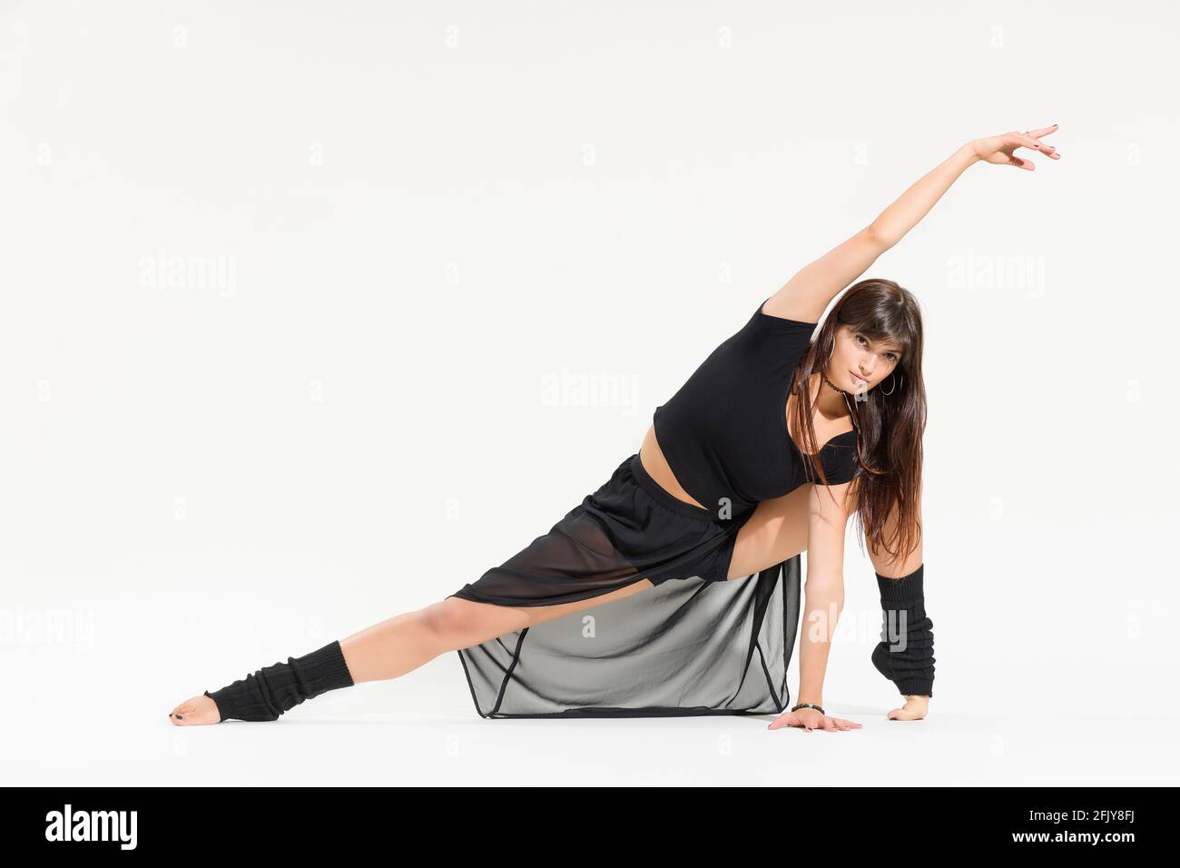 Supple young dancer doing a front stretch with flexed instep pose with raised arm while looking into the camera isolated on white with copyspace Stock Photo