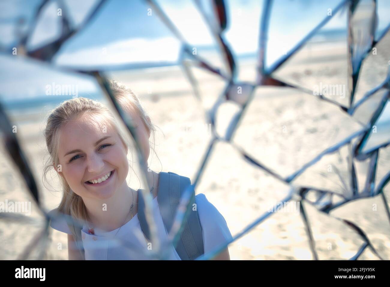 Reflection of a smiling blonde girl in a broken mirror - Stock Photo