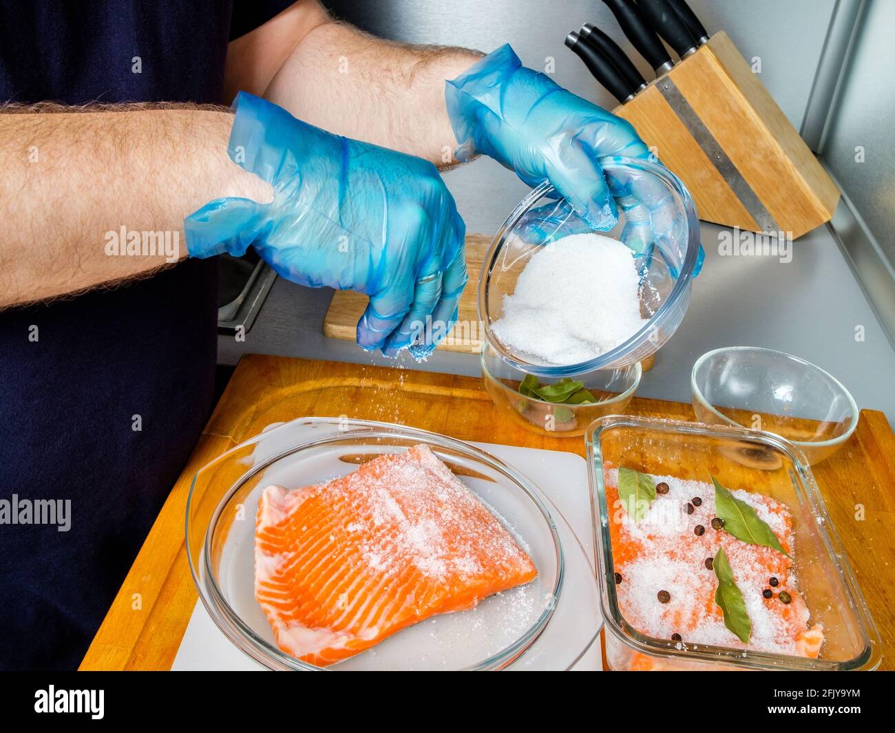 The hands of the cook in hygienic gloves sprinkle salmon fillets with